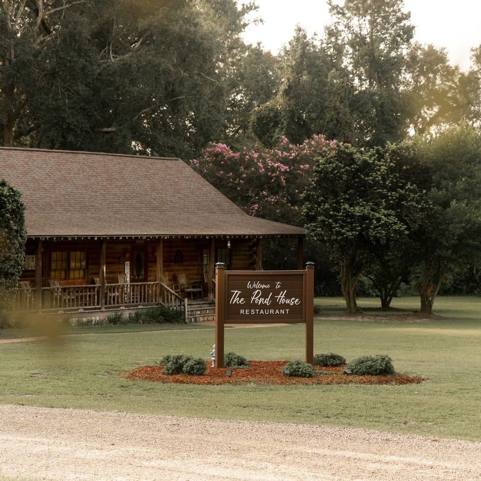 The Pond House welcome sign on the lawn with the cabin behind it