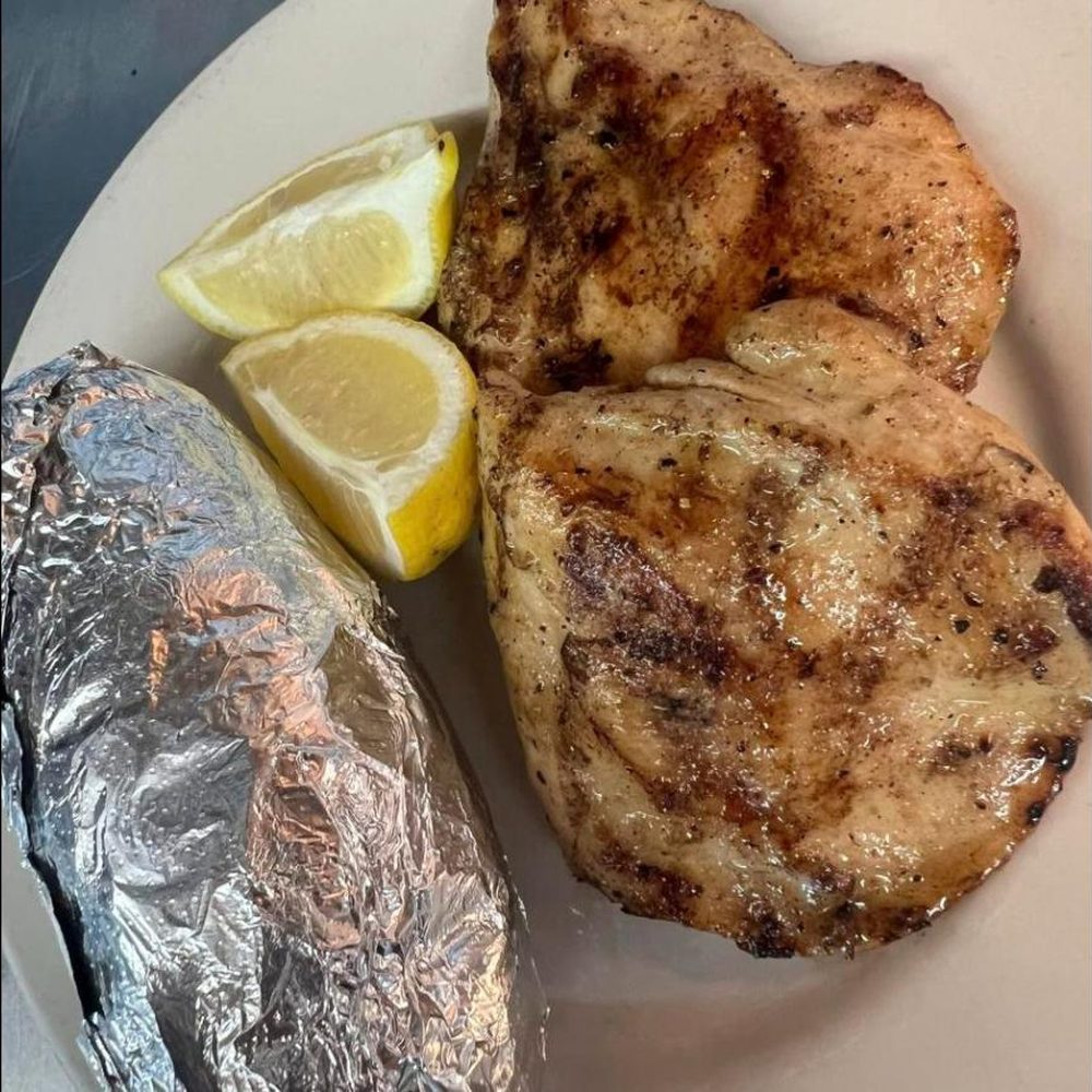 Two smoked pork chops with lemon and a foil-wrapped baked potato