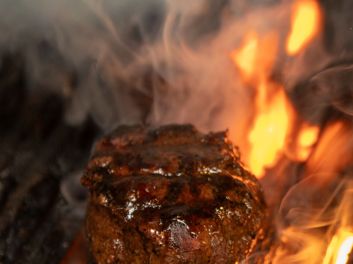A hand-cut steak searing over open flame on the charbroiler
